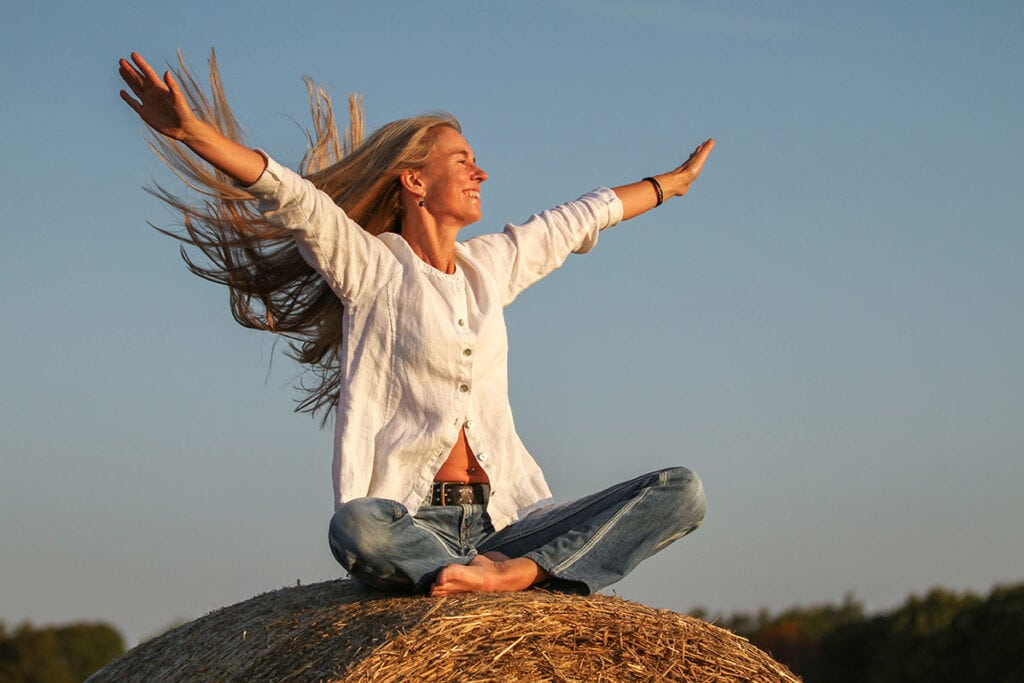 Kvinna på halmbal i morgonsol – fotograf Helena Silvertid